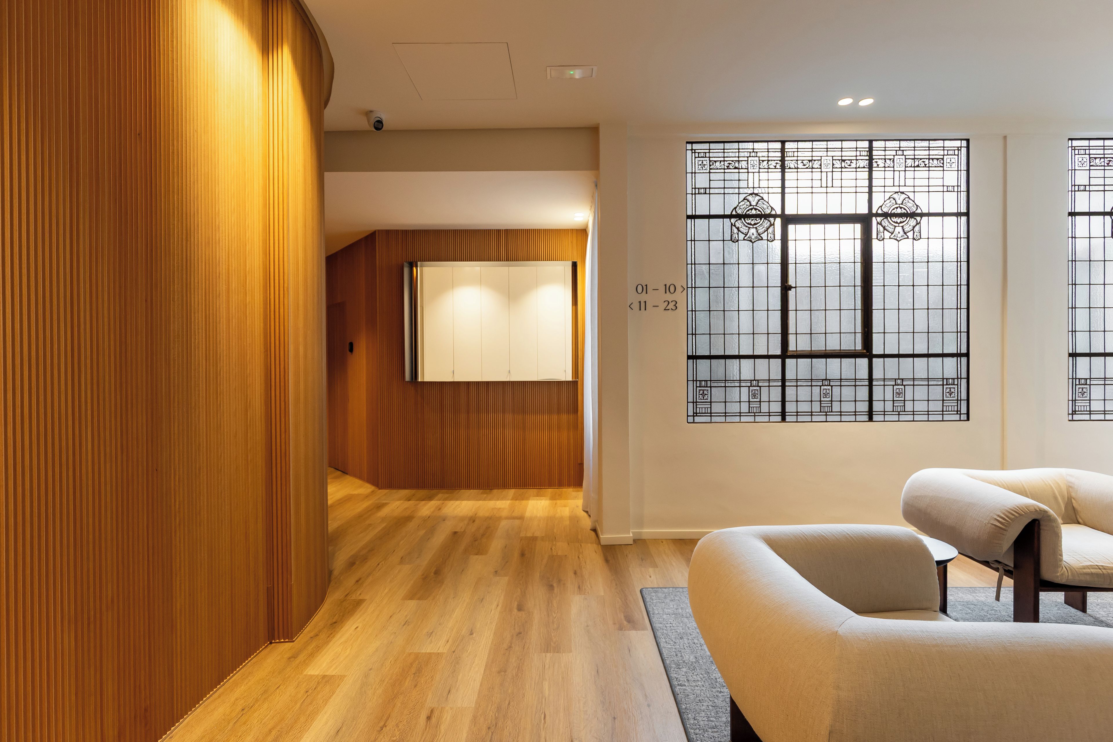 Un interior moderno con paneles de madera, suelo de madera, un sofá y una ventana con vidrio decorativo.