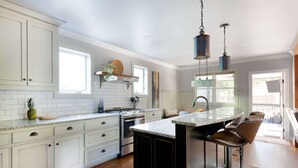 A kitchen with white cabinets, a central island with bar stools, a stove, and a hanging light fixture. - Silver Stallion (Atlanta)