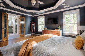 Une chambre à coucher avec un grand lit, une commode, une télévision et une fenêtre donnant sur les arbres.