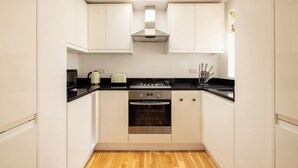 A compact kitchen with white cabinets, a black countertop, a stove, and an oven. - The Queenstown Villa (London)