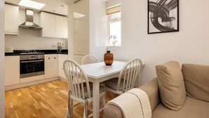A modern kitchen with white cabinets, a dining table with chairs, and a beige sofa. - The Queenstown Villa (London)