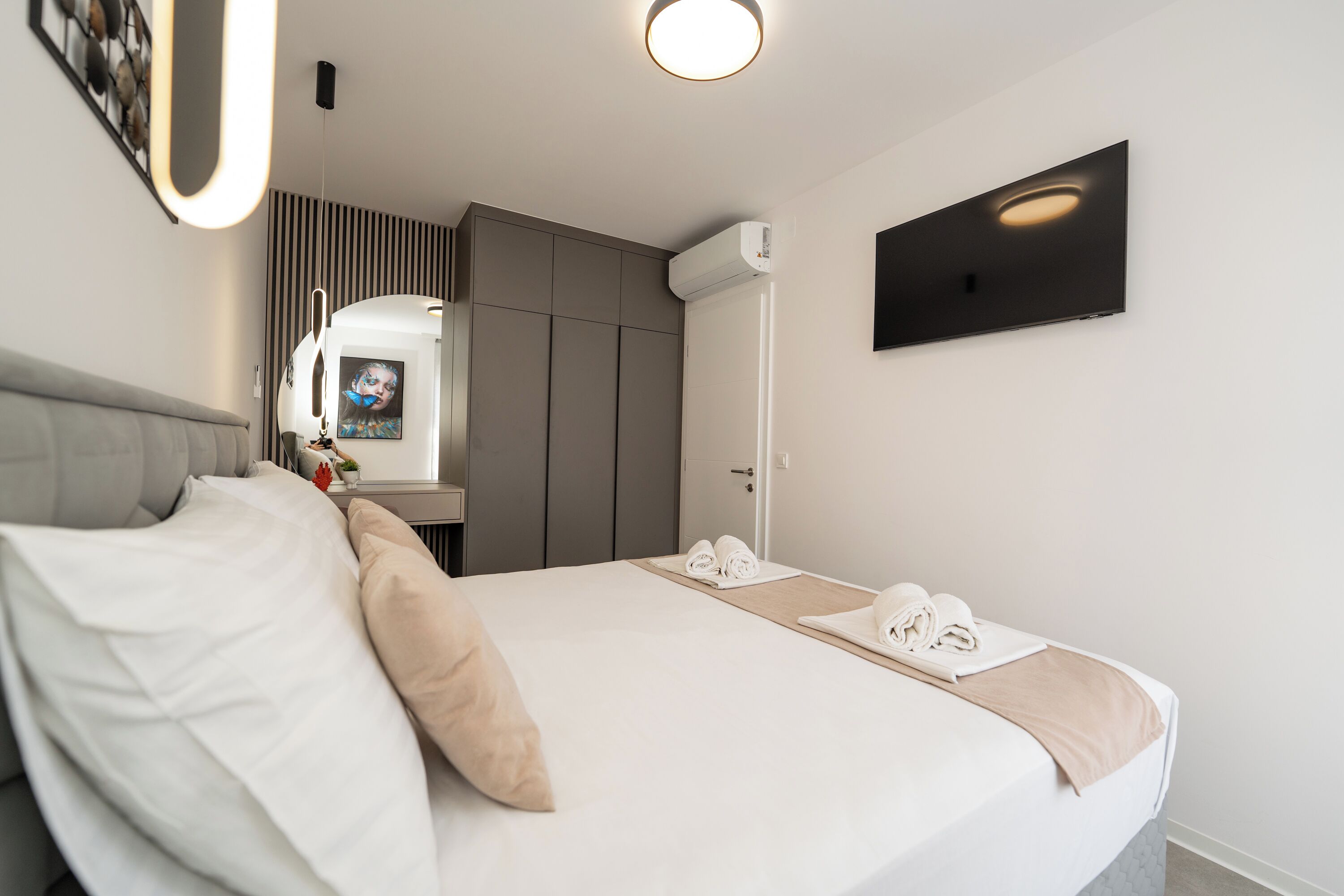 Et moderne hotelværelse med en stor seng, et fladskærms-tv på væggen og en aircondition-enhed.