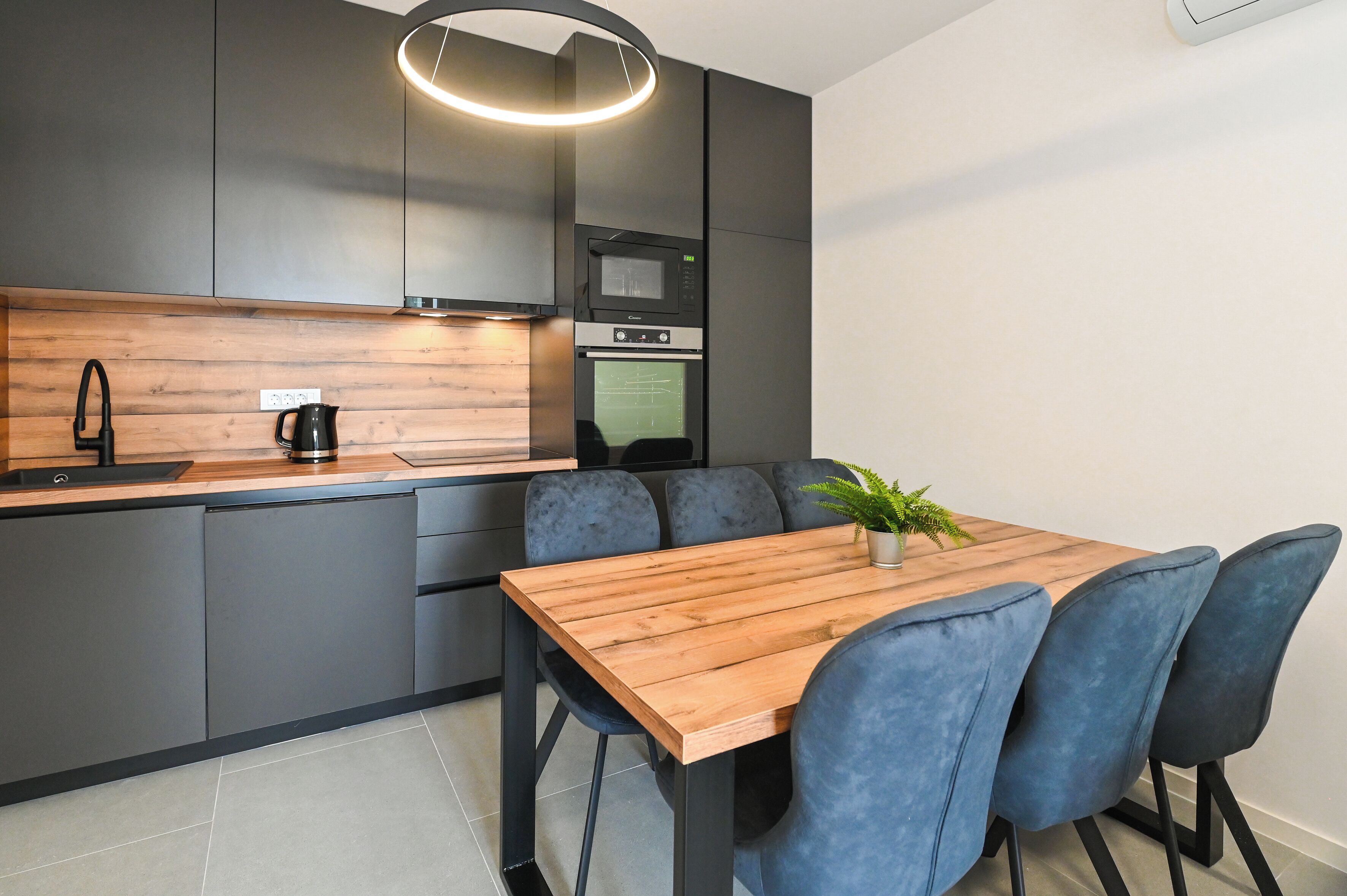 Une cuisine moderne avec des meubles gris, un plan de travail en bois, un four à micro-ondes encastré et une machine à café.