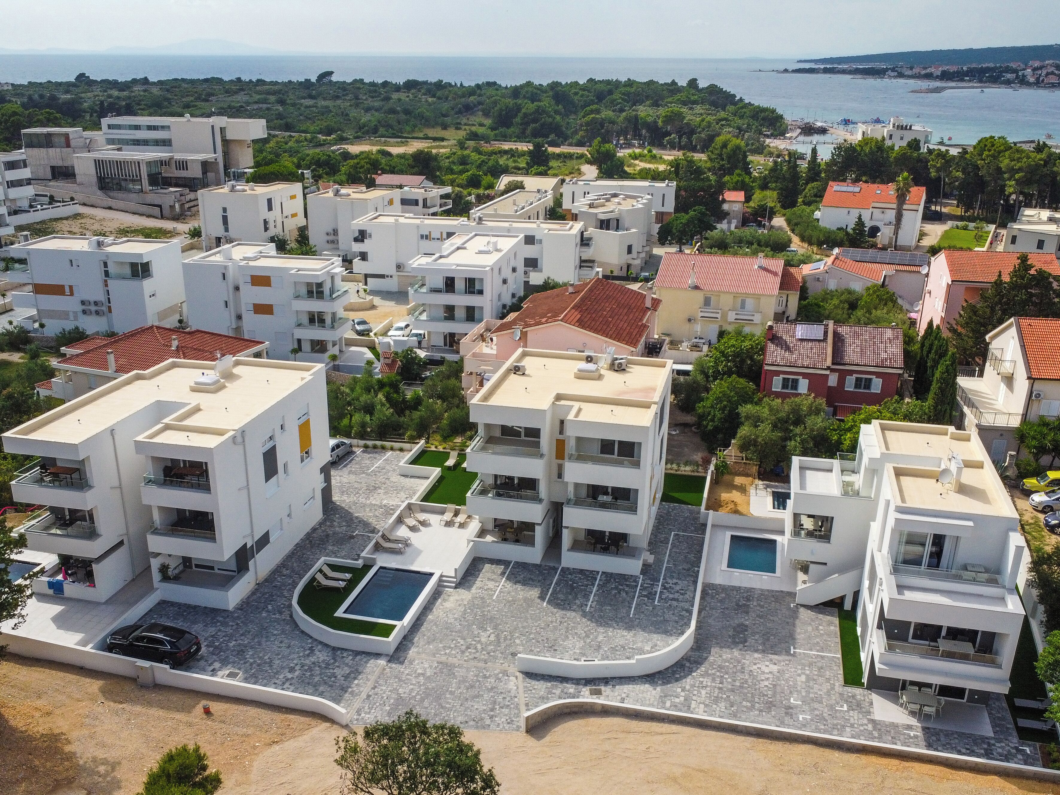 Una zona residenziale moderna con diversi edifici bianchi, una piscina e vista sul mare.