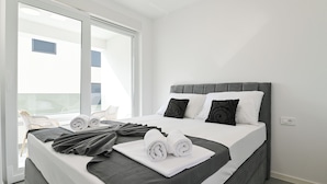 Een keurig opgemaakt bed met opgerolde handdoeken, een grijs hoofdbord en een wit kussen.