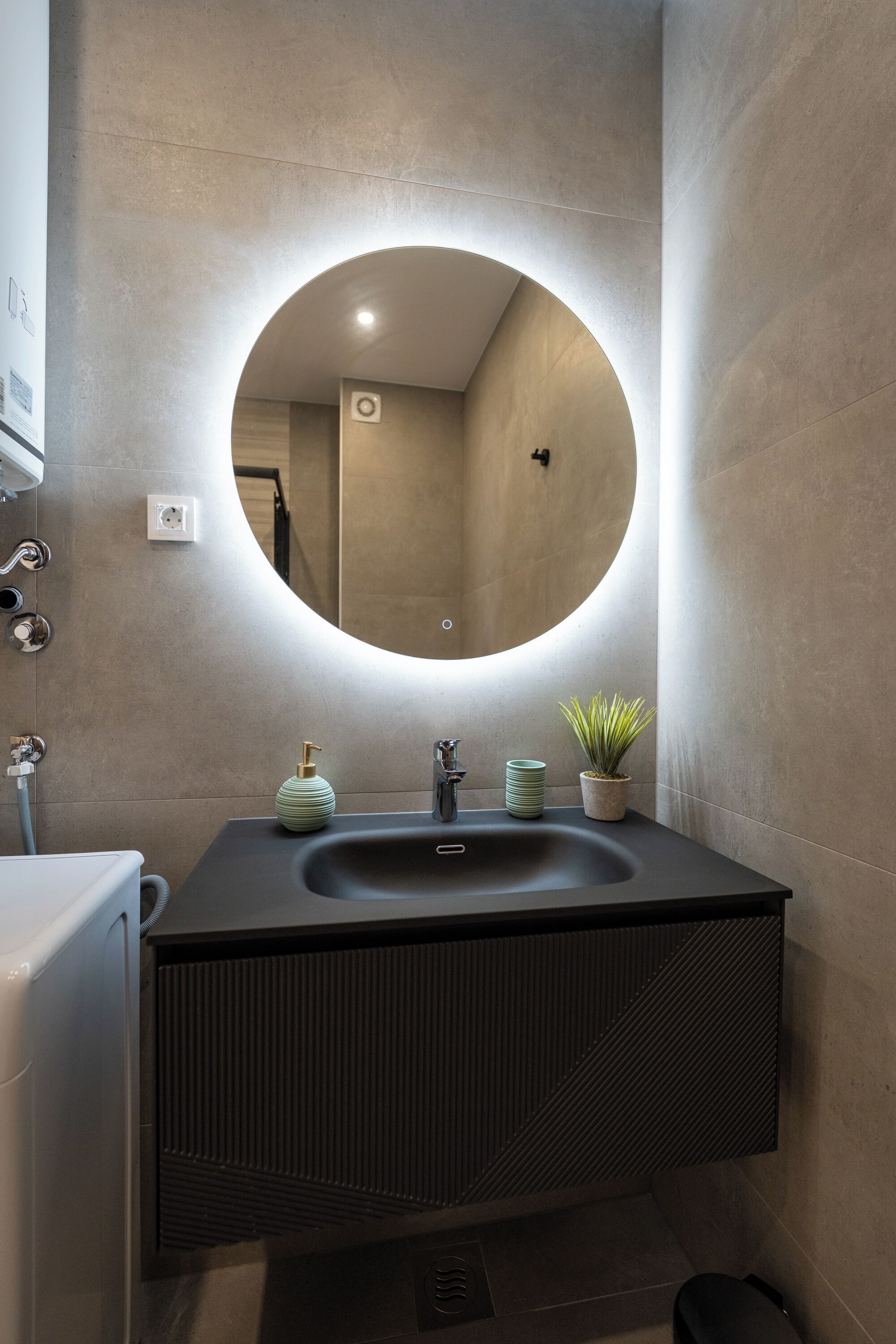 Un bagno moderno con uno specchio rotondo, un lavandino e una pianta in vaso.