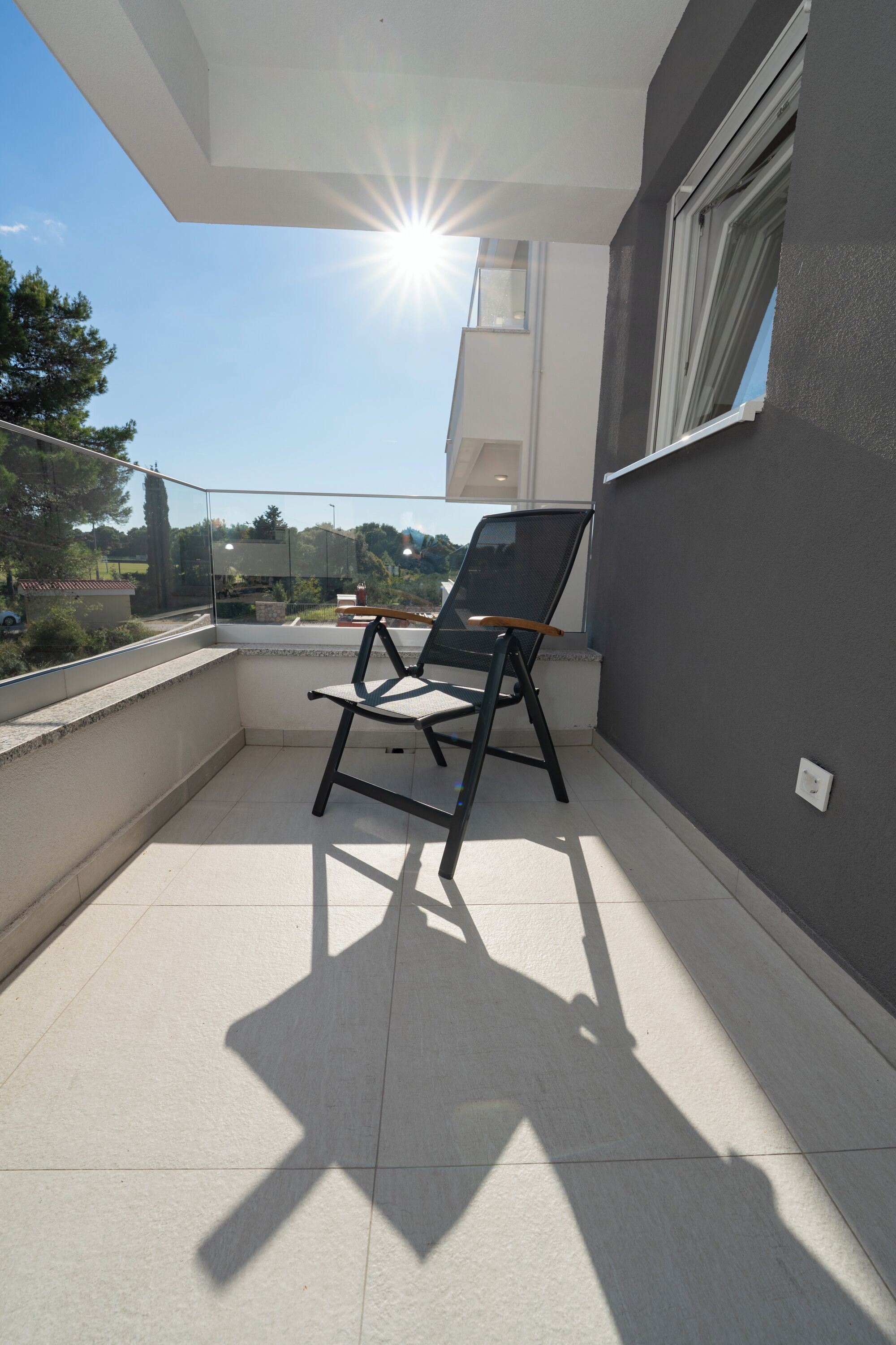 A balcony with a chair, a glass door, and a view of the surrounding area.