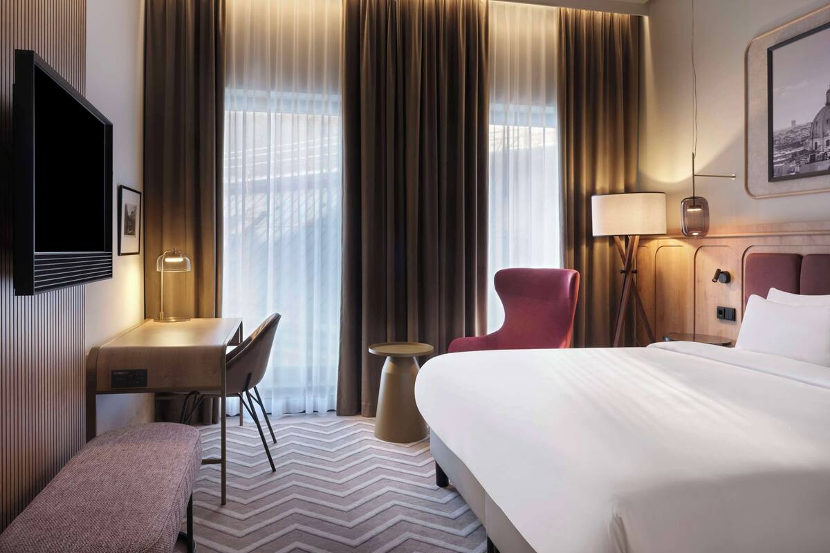 Ein Hotelzimmer mit einem Bett, einem Schreibtisch mit Stuhl, einem kleinen Tisch und einem Sessel.
