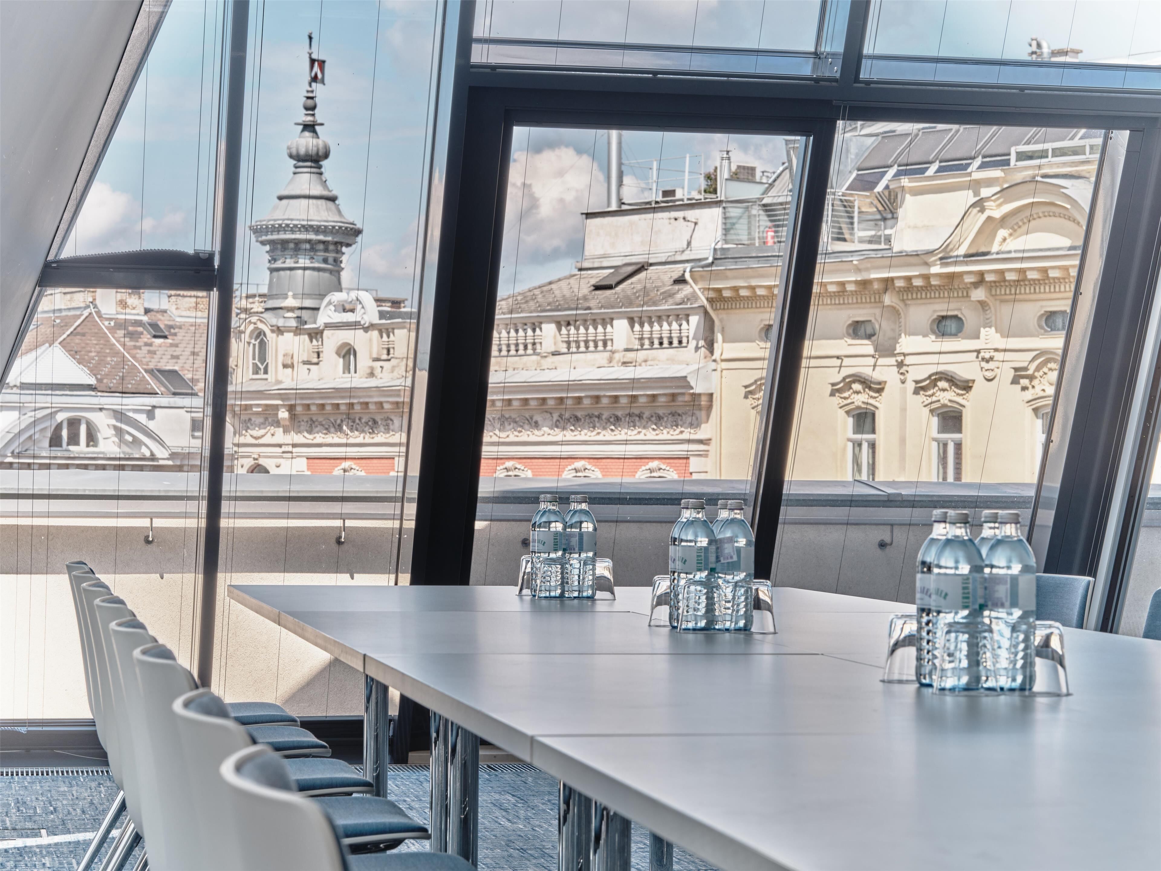 Un salón de conferencias con una mesa lista para reuniones, amplias ventanas que ofrecen vistas de arquitectura histórica.