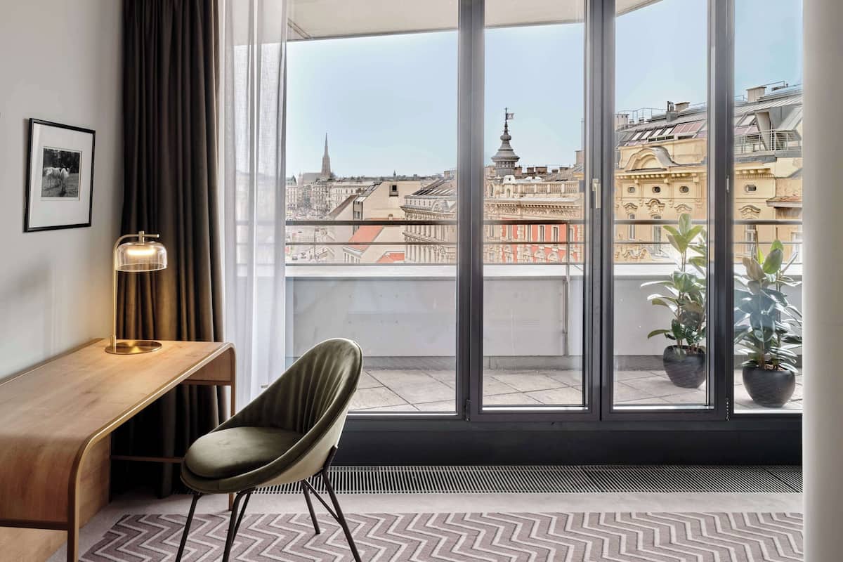 Ein modernes Zimmer mit großem Fenster, Schreibtisch, Stuhl und einer Zimmerpflanze.