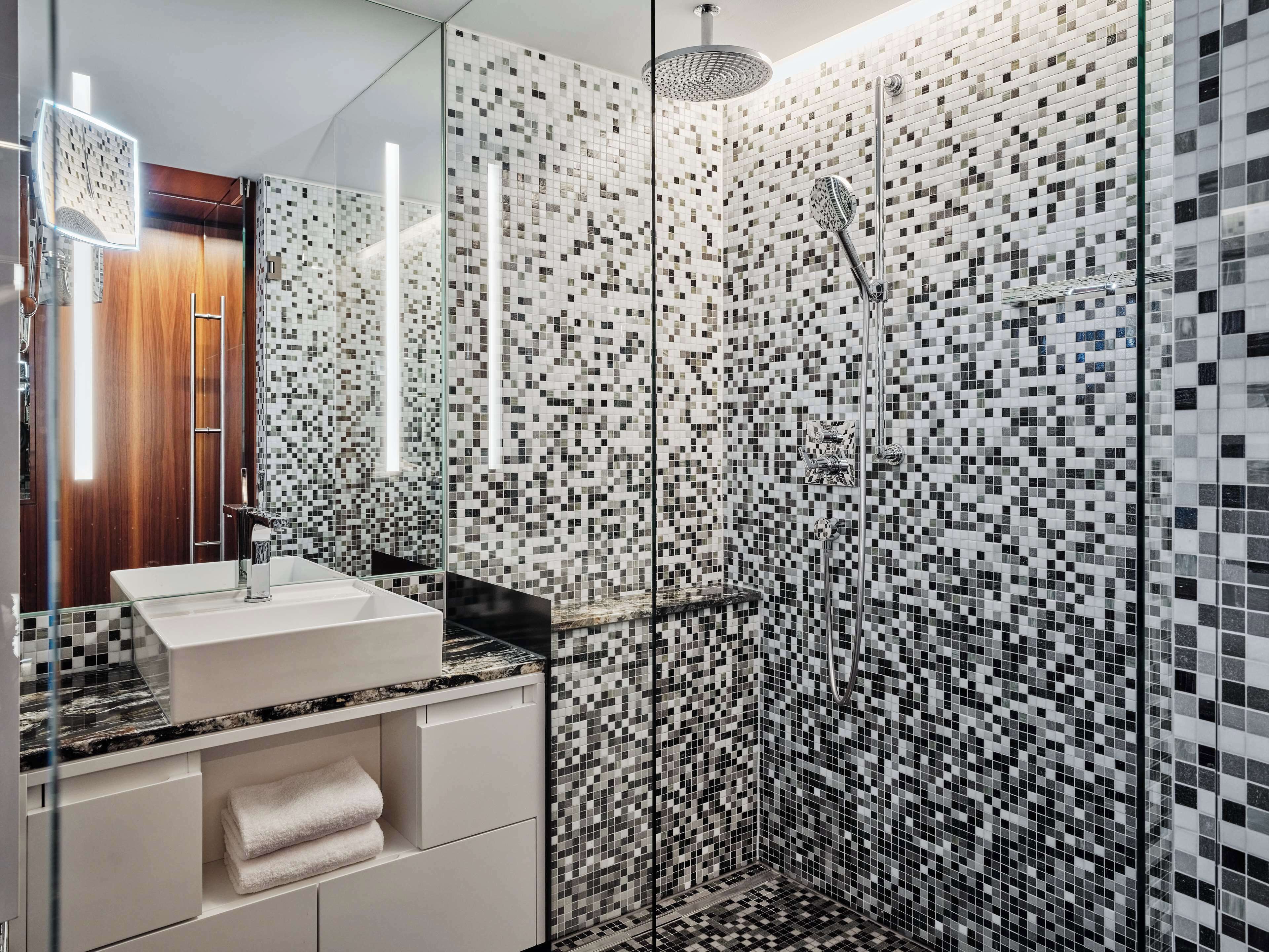 A modern bathroom with a glass shower enclosure, a white sink, and a wooden door.