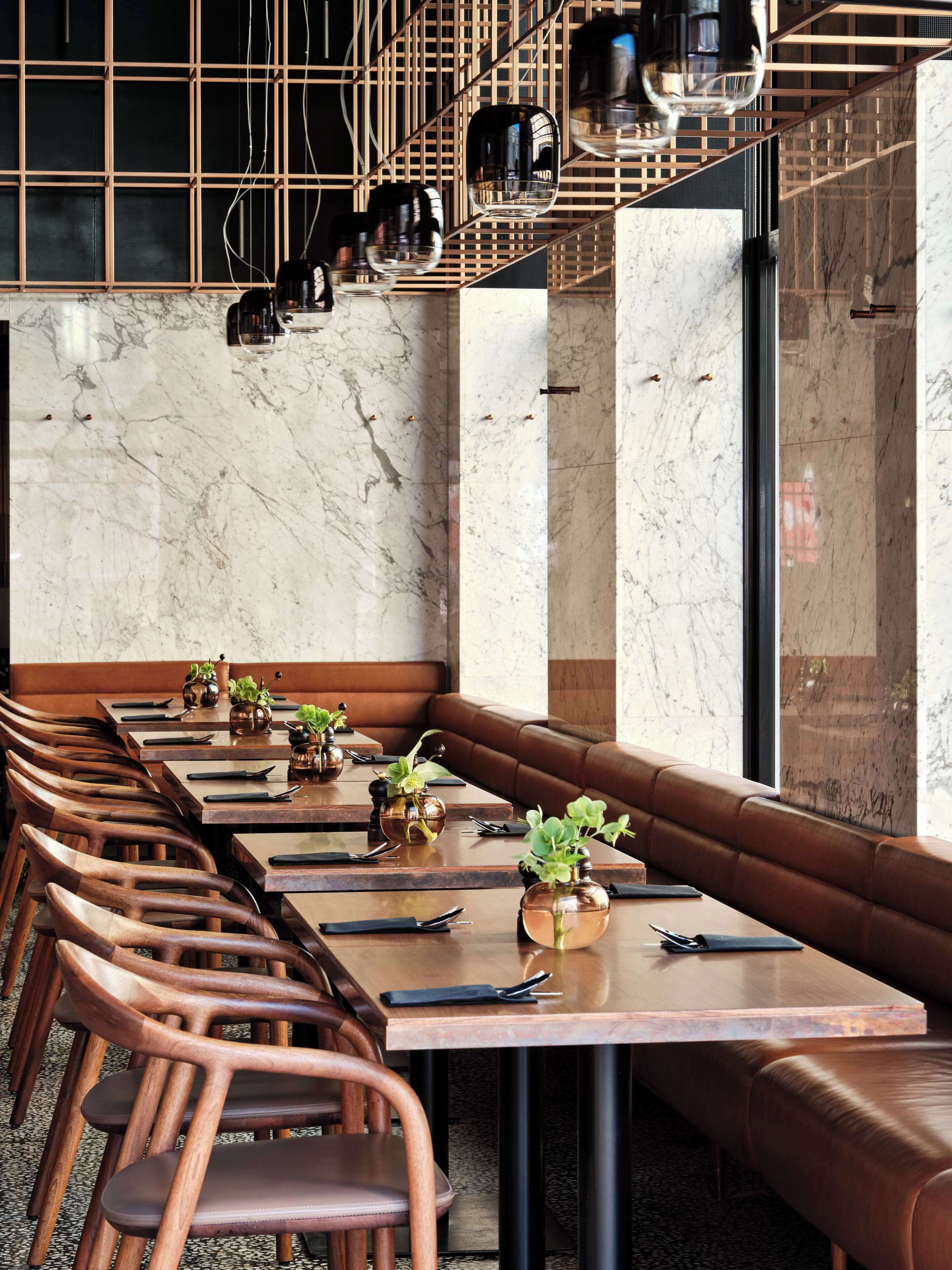 A modern dining area with marble walls, wooden tables, and leather booths.
