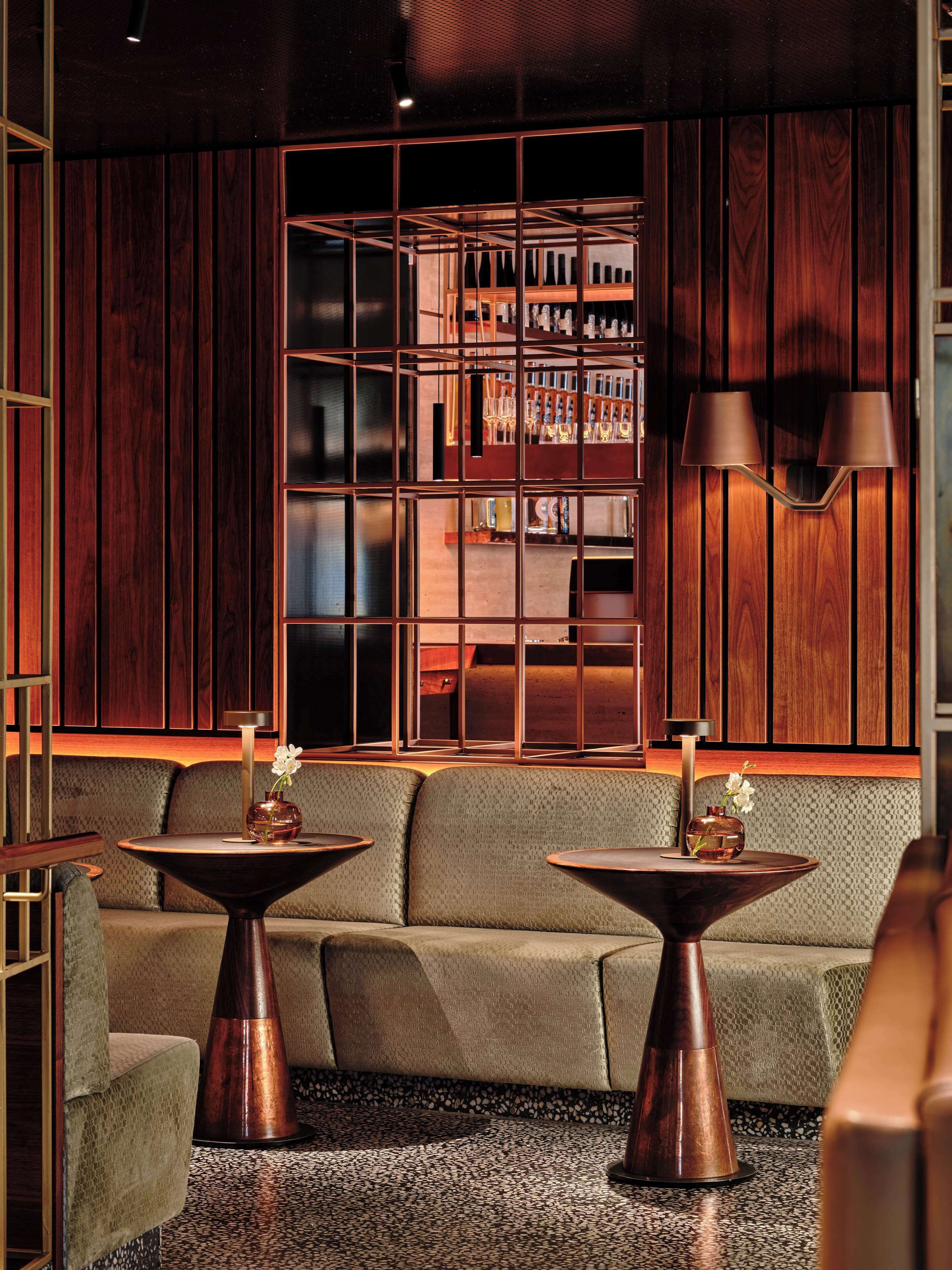 A modern interior with a wooden panel wall, two round tables with copper bases, and a seating area with a patterned sofa.