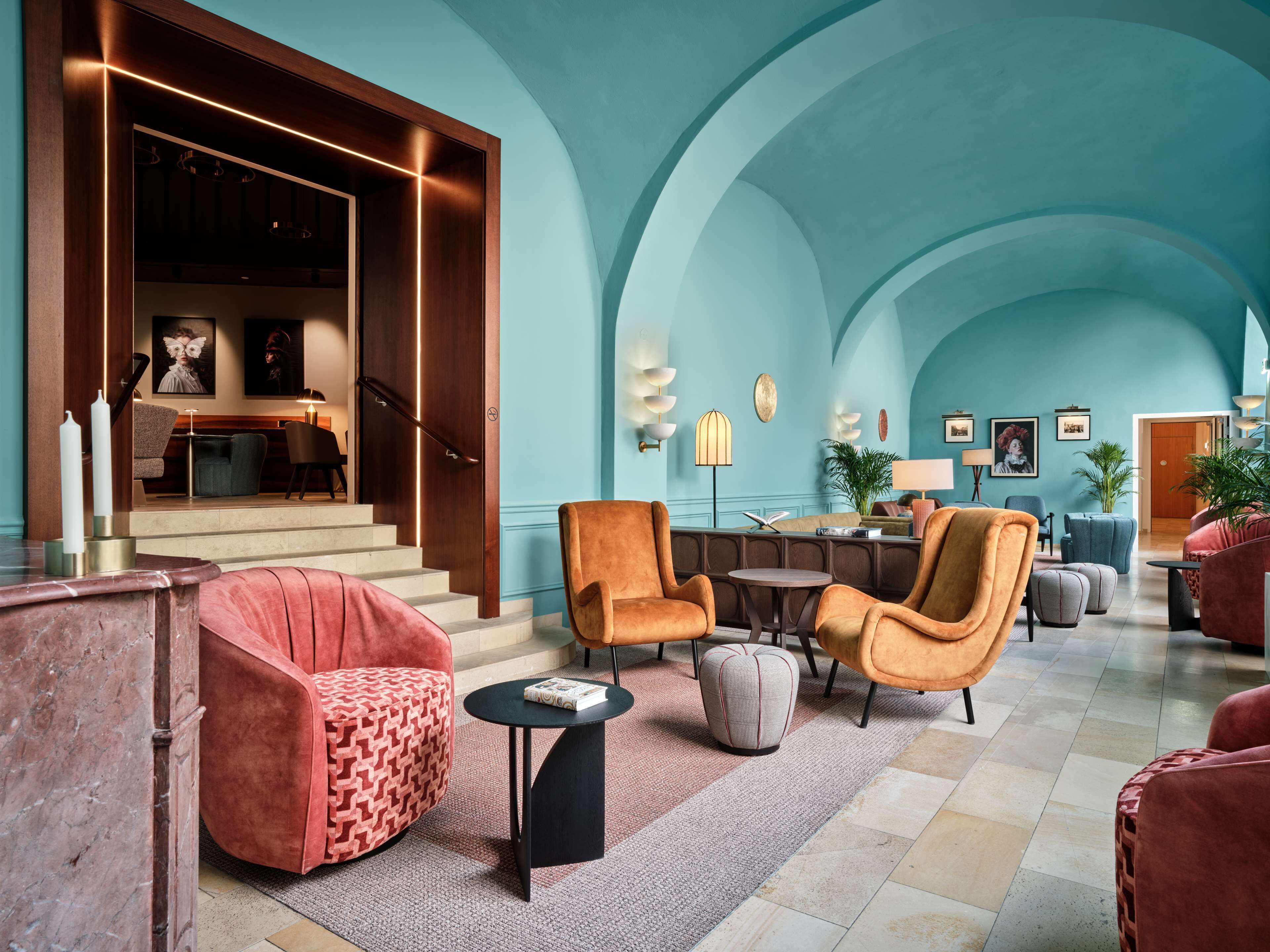 A spacious lobby with a high ceiling, a staircase leading to an upper floor, and a seating area with armchairs and ottomans.