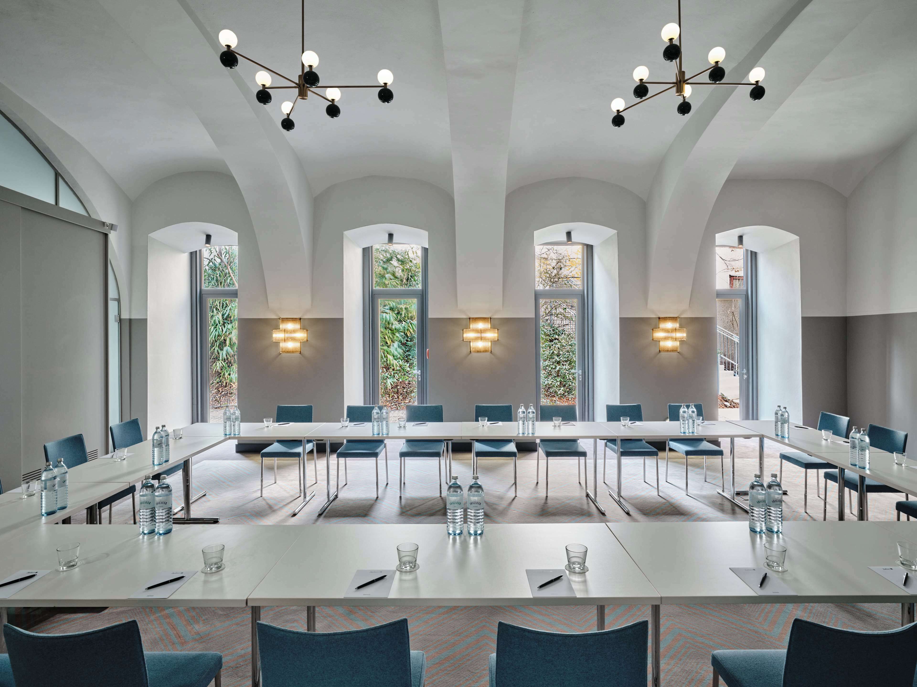 A conference room with a long table, chairs, water bottles, and a large window with a view of greenery.