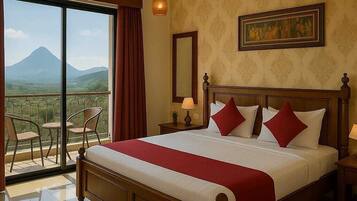 Habitación de hotel con una cama grande, ventilador de techo, balcón con sillas y vista a la montaña.
