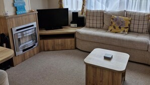 Una sala de estar acogedora con un televisor de pantalla plana, un aparador de madera, un sofá con cojines estampados y una mesita.