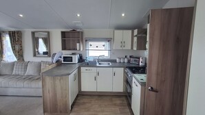 Una cocina compacta equipada con microondas, tostadora, pileta y cocina. Se observa un armario de madera y una ventana con cortinas.