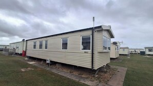 A single mobile home with a number 'MV62' on the side, a small porch, and a satellite dish. - Meadow View 3-bed Caravan - Sleeps 8 - Petfriendly (Skegness)