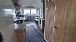 A narrow hallway leading to a kitchen and living area, with a wooden door on the right and a star decoration above it. - Meadow View 3-bed Caravan - Sleeps 8 - Petfriendly (Skegness)