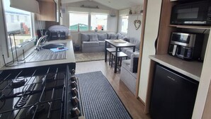 A compact kitchenette with a gas stove, microwave, and coffee maker. - Meadow View 3-bed Caravan - Sleeps 8 - Petfriendly (Skegness)