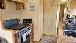 Eine kompakte Küchenzeile mit Herd, Backofen und Spüle. Holzschränke und eine Sternen-Dekoration sind an der Wand zu sehen.