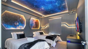 Un dormitorio con dos camas, un techo decorado con un mural de galaxia y un televisor montado en la pared.