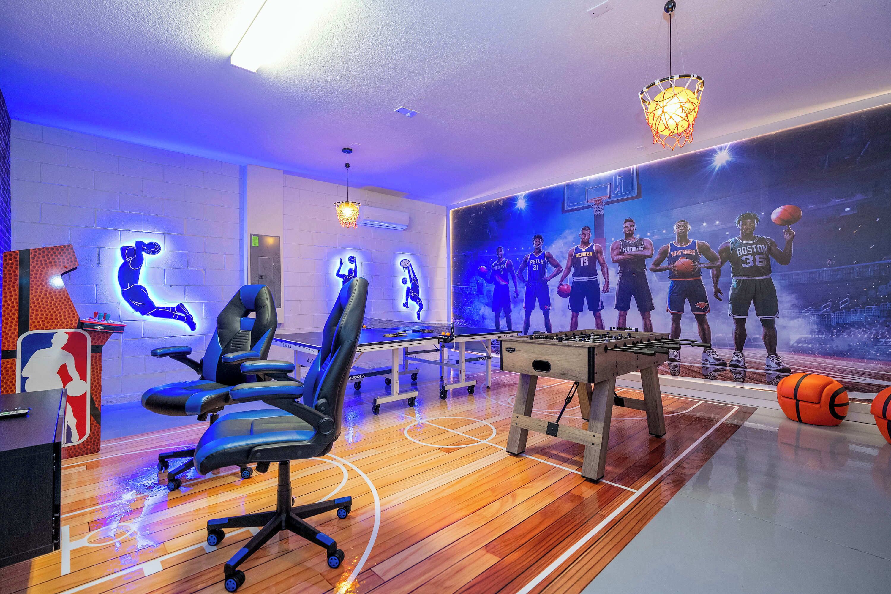 A basketball-themed room with a wooden floor, a foosball table, a desk with a computer, and a wall mural of basketball players.