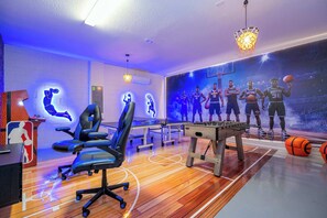 A basketball-themed room with a wooden floor, a foosball table, a desk with a computer, and a wall mural of basketball players. - 7392 Luxury Family Home 5BD Near Disney! (Davenport)