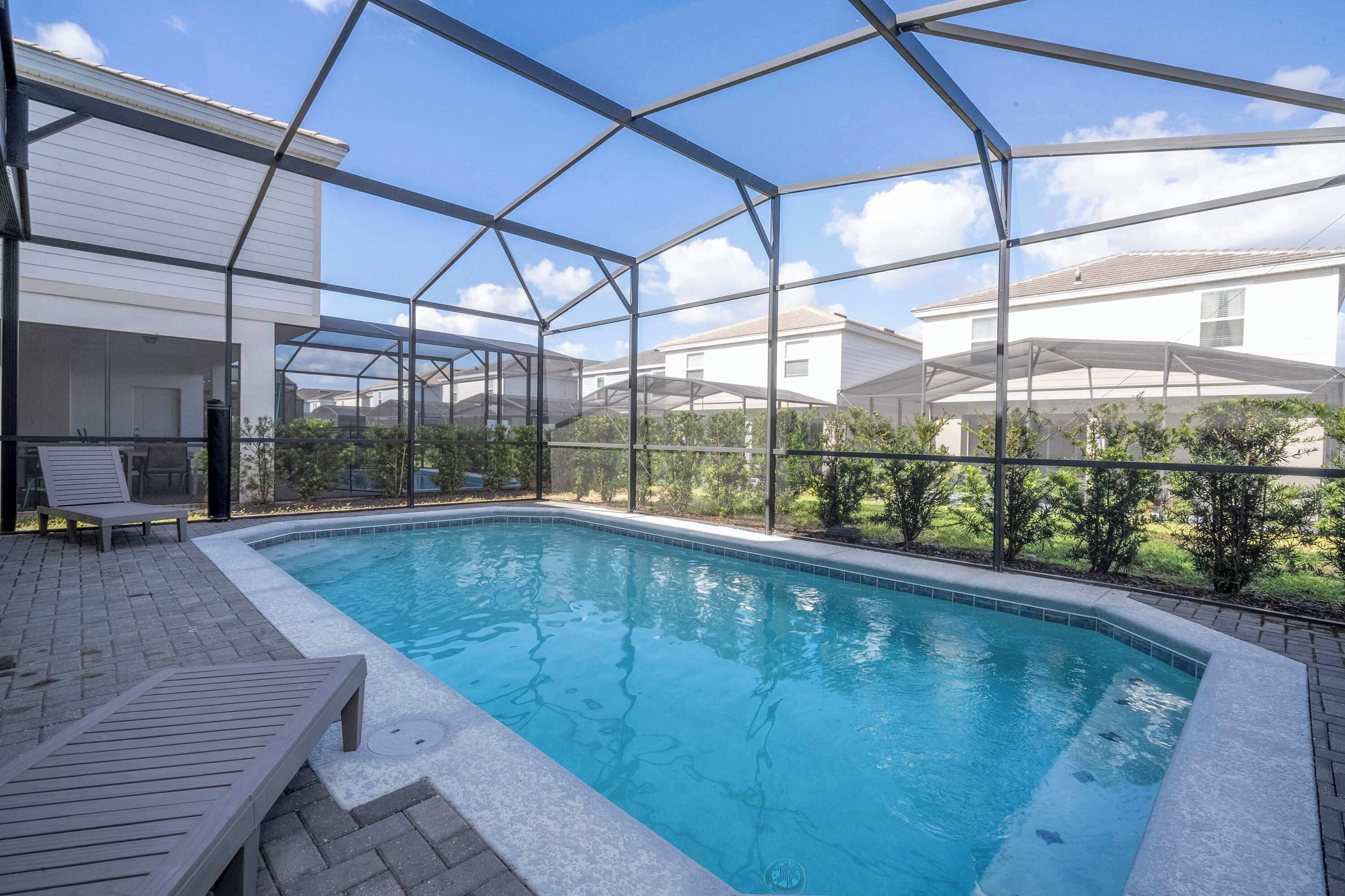 Une piscine dotée d ’une enceinte en verre, entourée d’un espace patio aménagé avec des chaises longues.