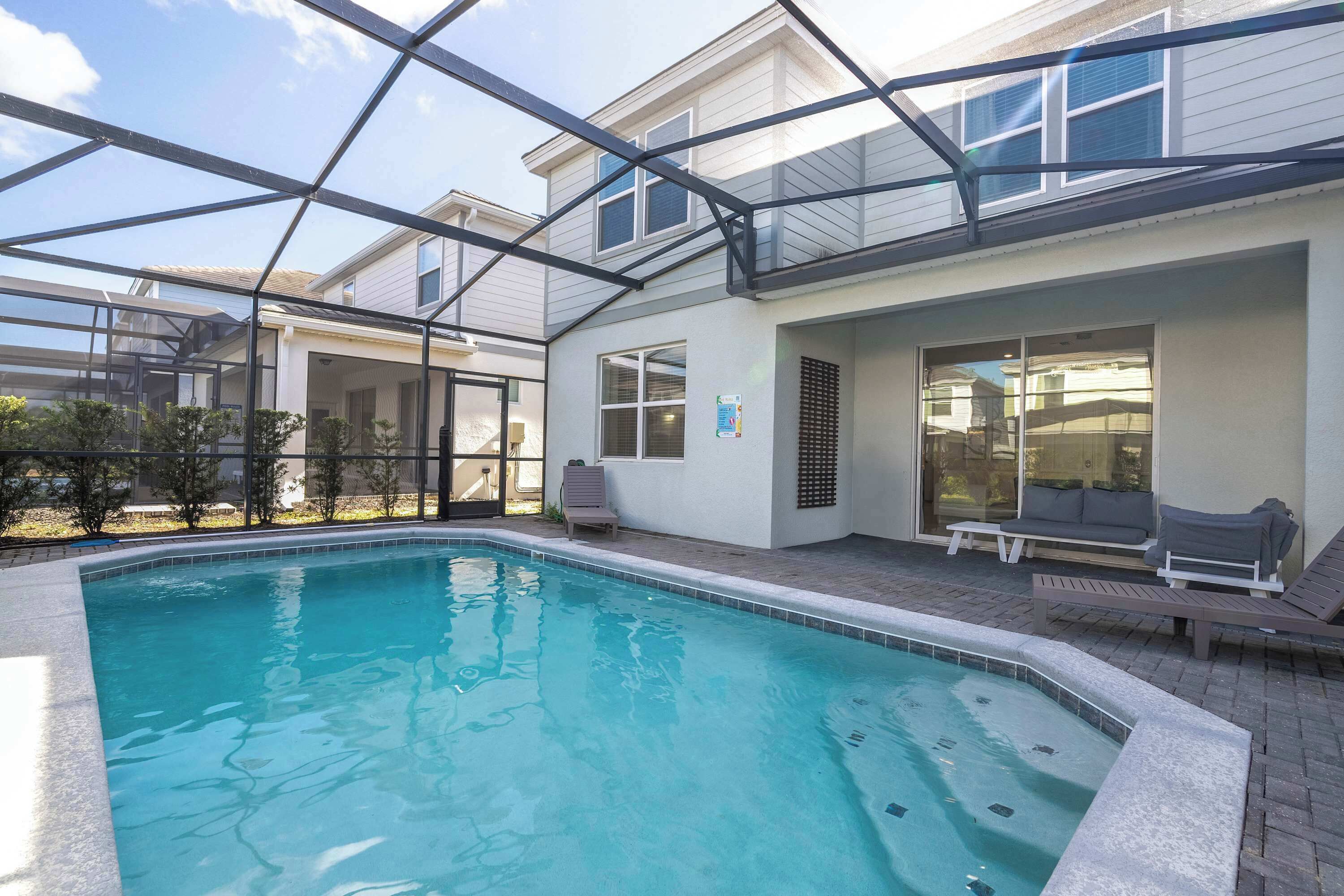 A swimming pool with a glass enclosure, a patio area with seating, and a building with large windows.
