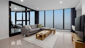 A modern living room with a sofa, coffee table, TV, and large windows offering a city view.