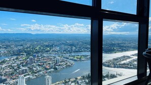 A panoramic view from a high-rise window overlooking a cityscape with a river, buildings, and distant mountains.