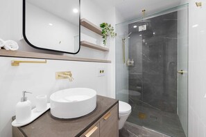 Sink, mirror, and shower area with gold accents and white tiles.