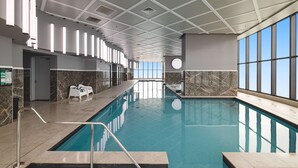 An indoor swimming pool with a tiled floor, a marble wall, and a ceiling with a grid pattern.