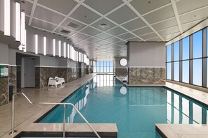 An indoor swimming pool with a tiled floor, a marble wall, and a ceiling with a grid pattern.