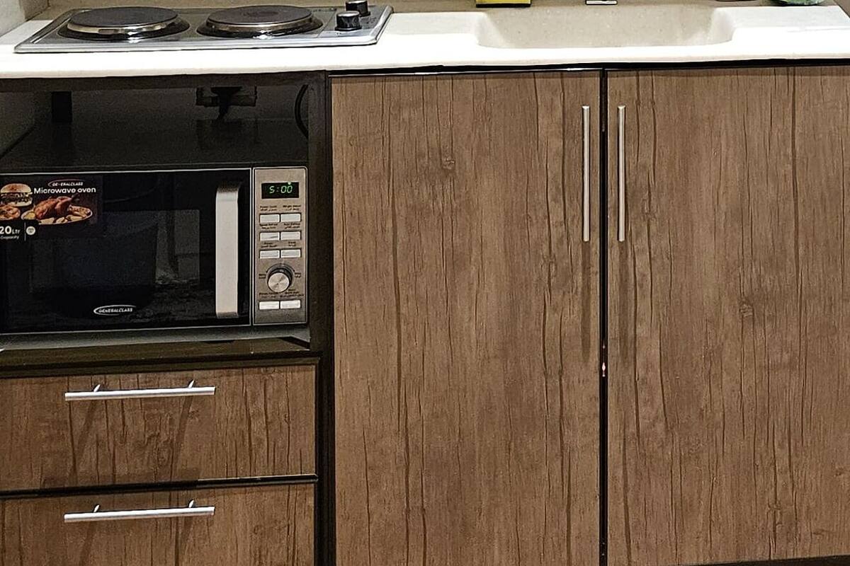 A kitchen with a microwave, stove, and a small cabinet with a tray of toiletries.