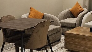 Ein modernes Wohnzimmer mit einem grauen Sofa, zwei Sesseln, einem Holztisch und einem kleinen Tisch mit einer Taschentuchbox.