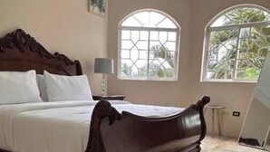 A bedroom with a large wooden bed, two arched windows, and a tiled floor.