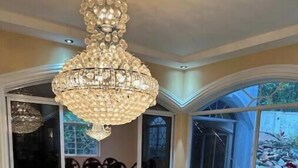 A spacious living room with a yellow sofa, a large chandelier, and a view of a garden through the glass doors.