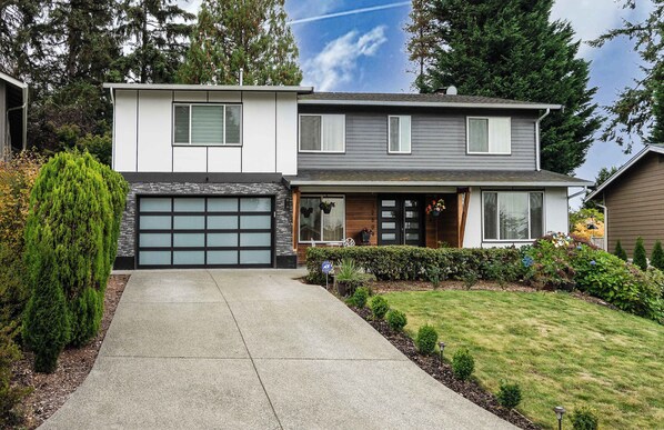 Une maison moderne à deux étages, dotée d’un garage, d’une pelouse bien entretenue et d’une variété d’arbustes et d’arbres.