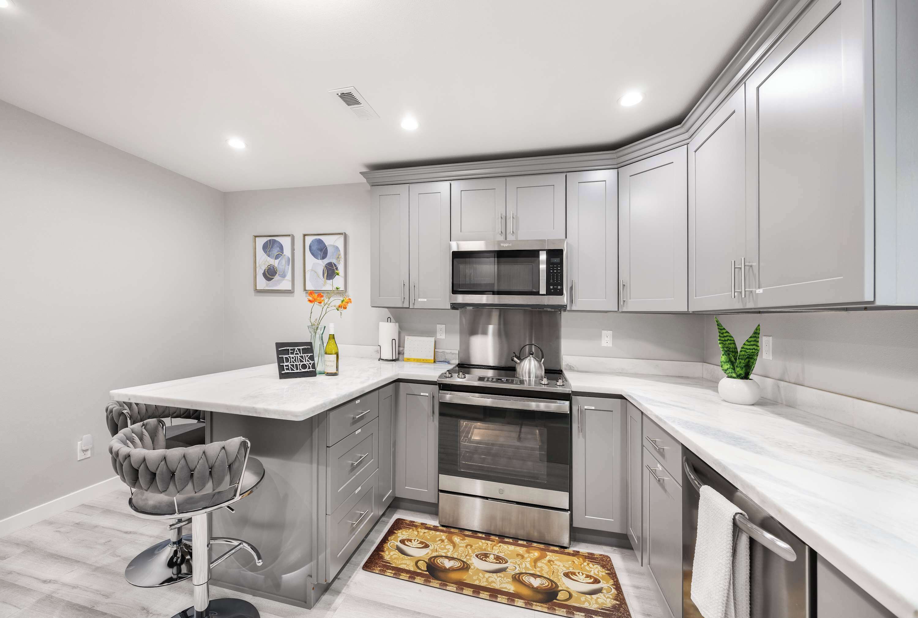 Una cocina moderna con armarios grises, un horno de acero inoxidable, un microondas y una barra con una silla tapizada en gris.
