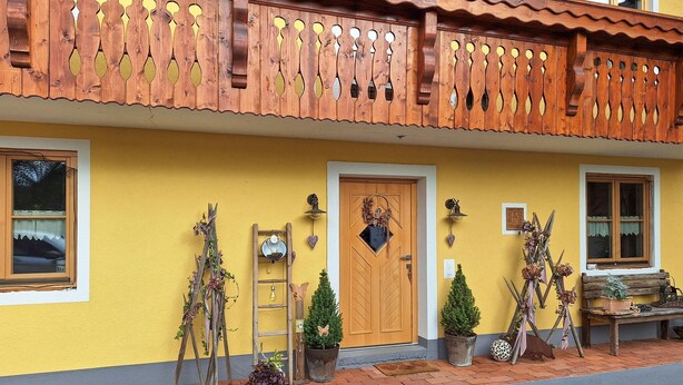 Un bâtiment jaune avec un balcon en bois, une porte en bois et diverses plantes en pot.