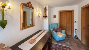 Un couloir avec un banc en bois, un fauteuil bleu, un miroir et une statue.