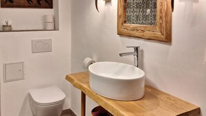 Une salle de bain avec des toilettes blanches, un meuble-lavabo en bois avec un lavabo blanc et un miroir encadré.