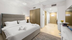 Een moderne hotelkamer met een groot bed, een nachtkastje met een lamp, een garderobe, een spiegel en een klein bureau met een bloemenvaas.