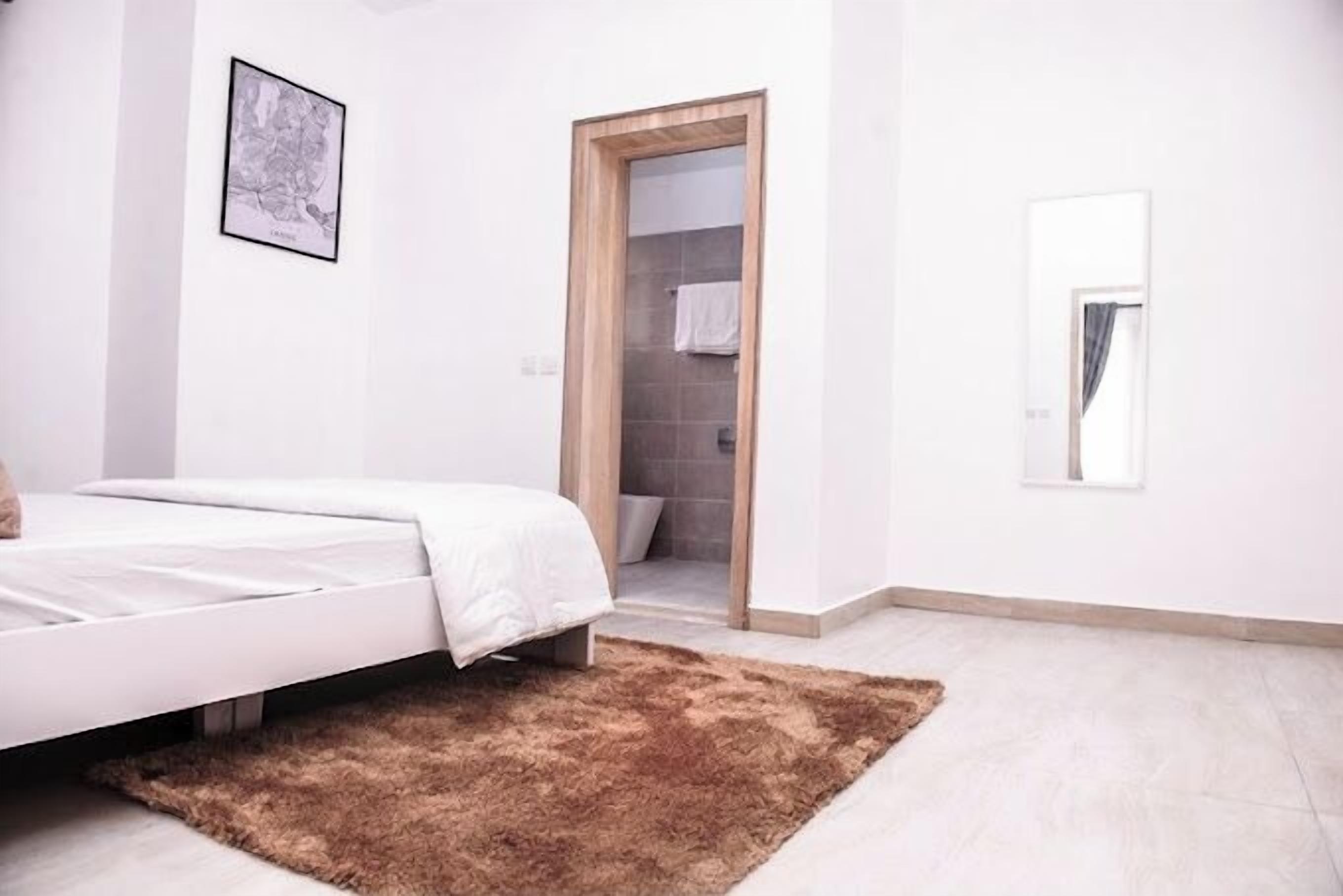 Une chambre à coucher avec un lit, un tapis marron, un tableau encadré au mur et une porte donnant sur une salle de bain.