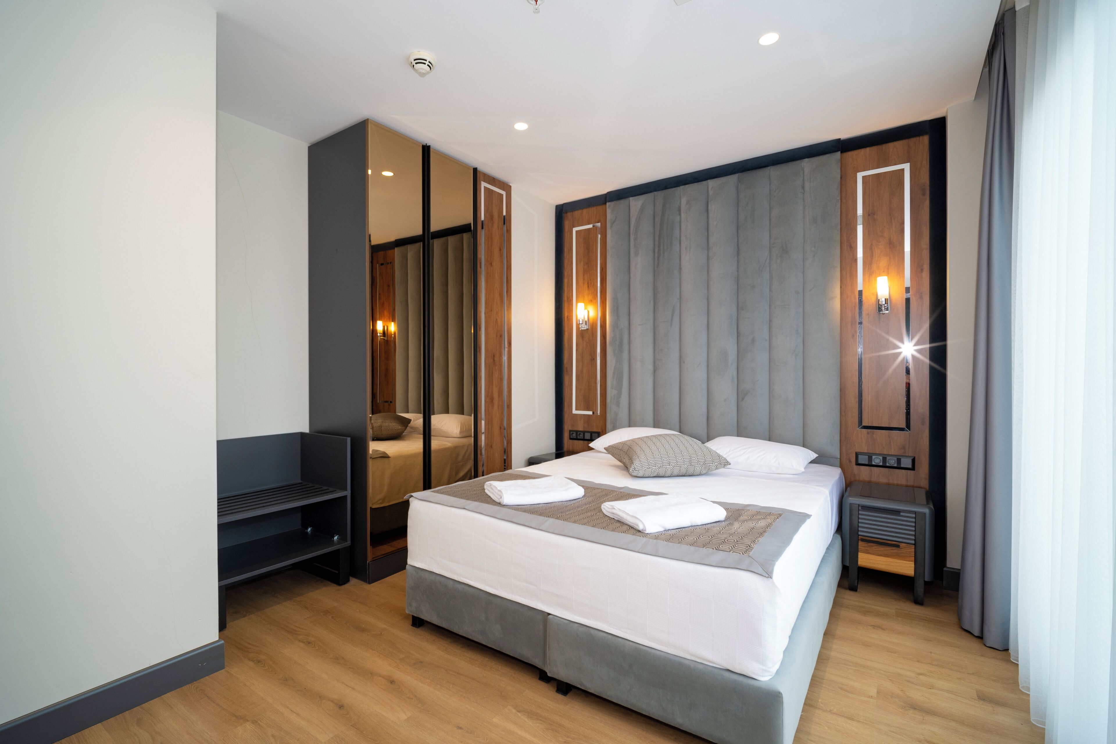 Una habitación de hotel moderna con una cama grande, un área de descanso, un espejo y una mesita de noche.