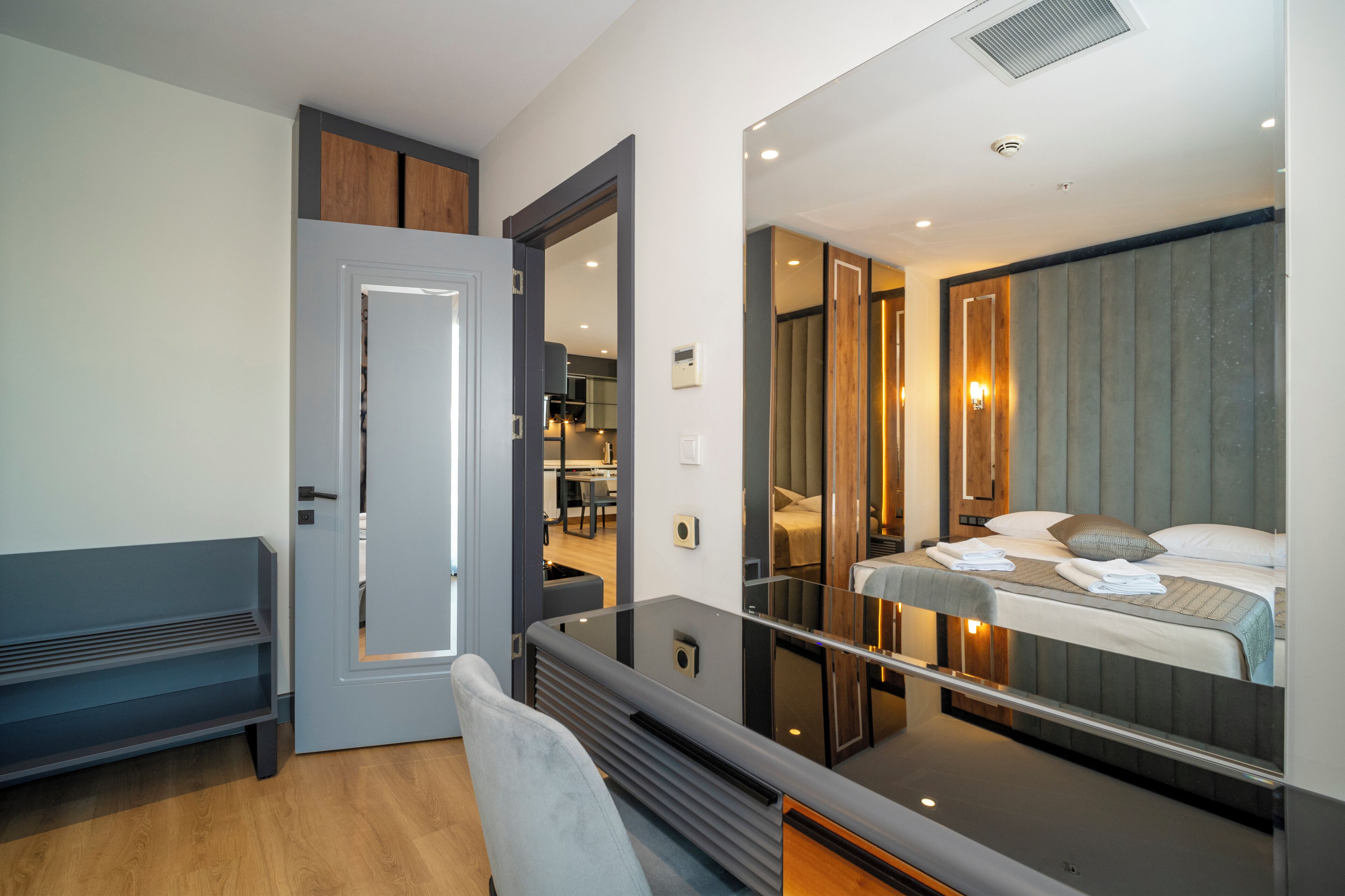 A modern hotel room with a large mirror, a bed, a desk, and a bench.