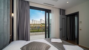 Ein modernes Hotelzimmer mit einem großen Bett, einem Balkon mit Blick auf die Stadt und einer Tür zu einem weiteren Raum.